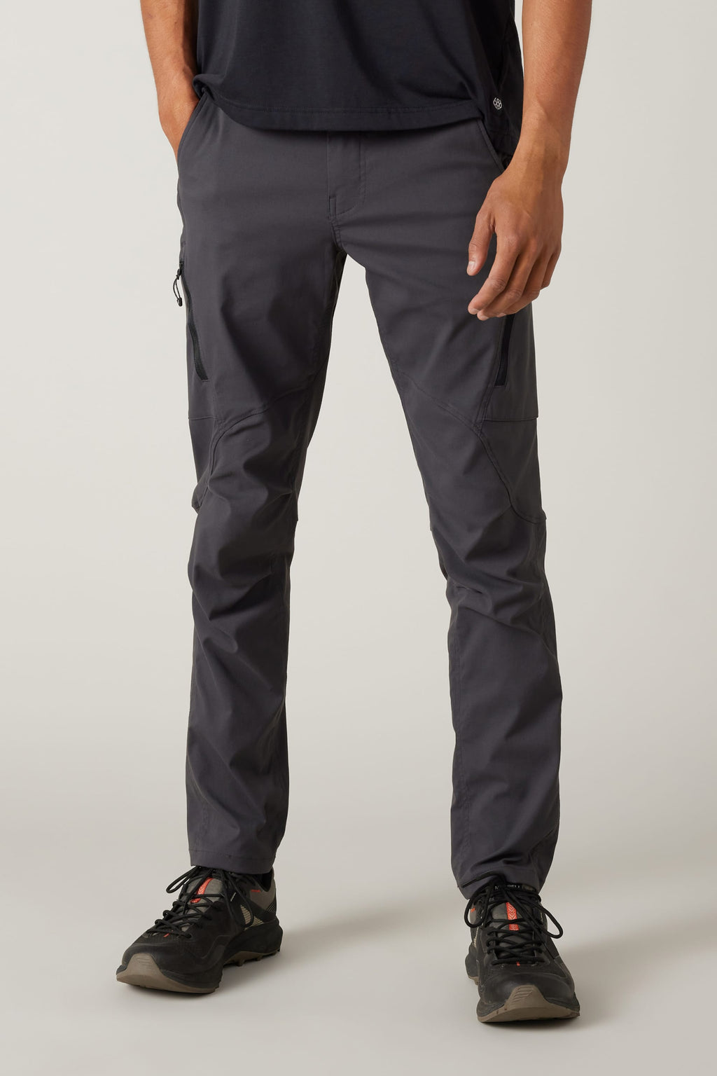 A person wears 686 Men's Anything Cargo Pant - Slim Fit in dark gray, featuring 13 utility pockets, paired with a black shirt and black athletic shoes. The shot focuses on the lower half against a plain light background, ready for any adventure.