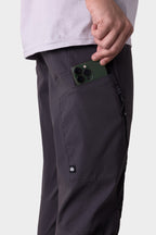 A person in 686 Men's Anything Cargo Pant - Slim Fit, dark gray with a branded patch above the side pocket, slips a green smartphone inside. Only their lower torso and arm are seen—pants built for adventure from 686.
