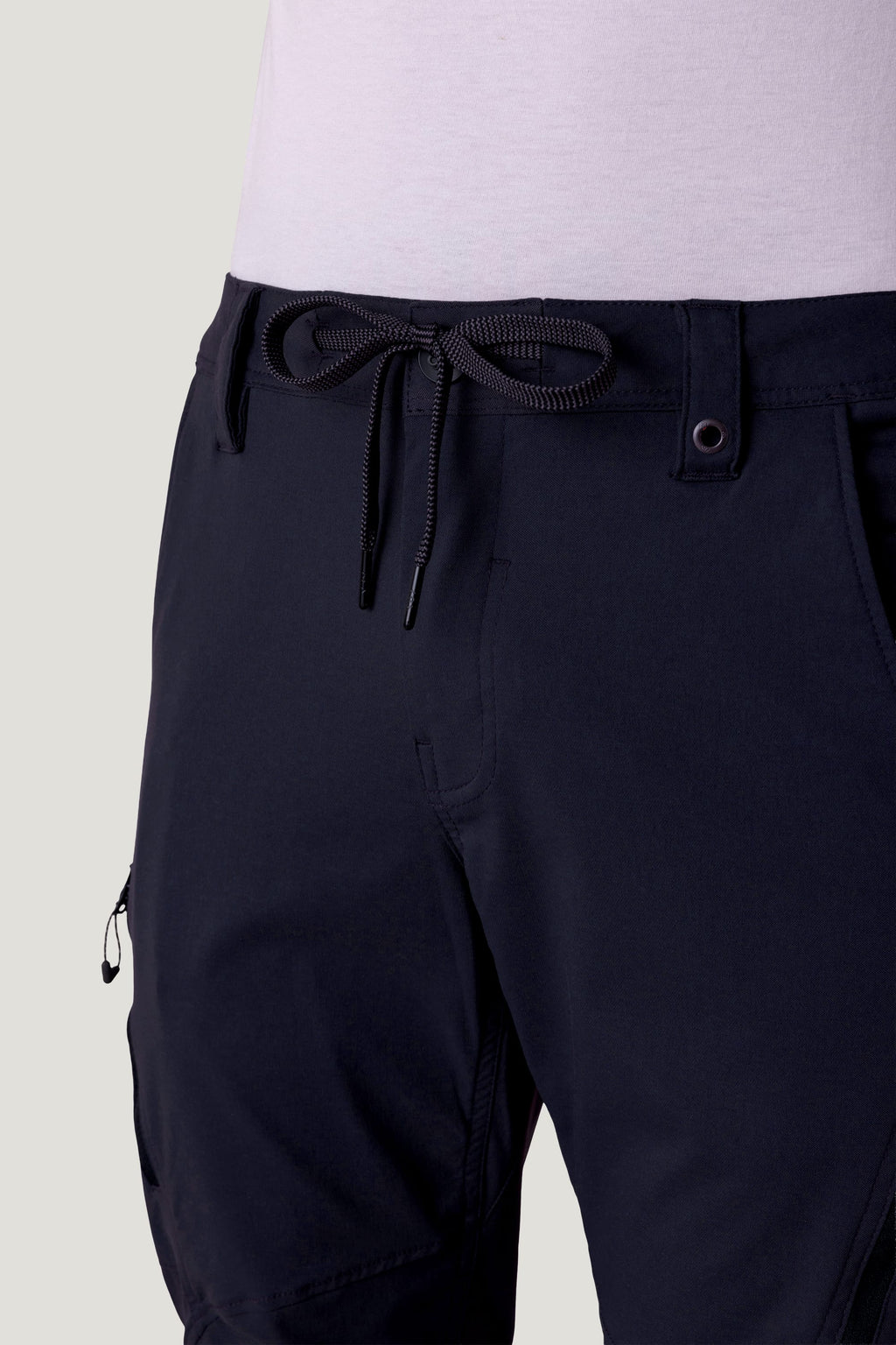 Close-up of a person wearing 686 Men's Anything Cargo Pant - Slim Fit by 686, featuring a drawstring waist and adventure-ready 13-pocket details at the waist and sides with a light-colored shirt tucked in.