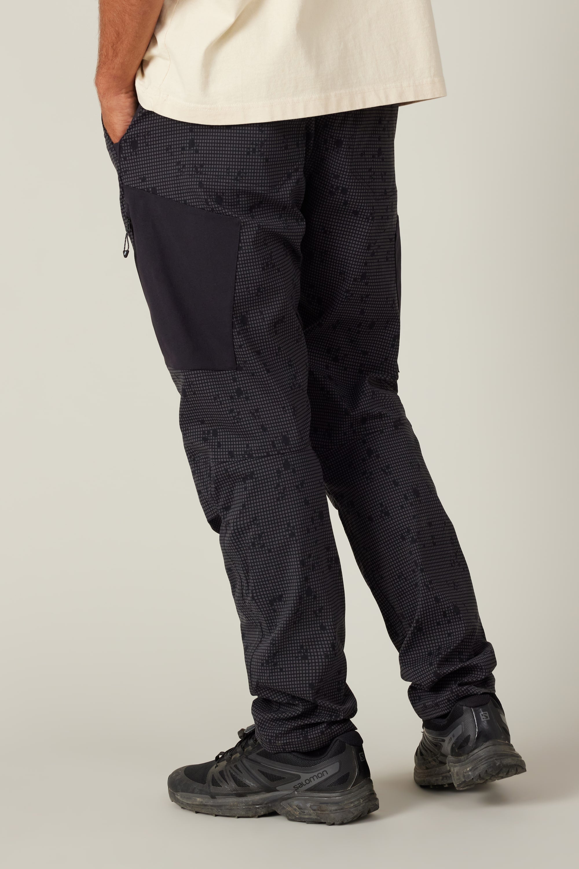 A person in 686 Men's Anything Cargo Pant - Slim Fit (13-pocket), paired with black sneakers, stands with one leg slightly bent, photographed from behind against a plain background—ready for any adventure.
