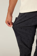 A person wearing 686 Men's Anything Cargo Pant - Slim Fit is unzipping a side pocket on their thigh with one hand; only their lower torso and hand are visible.