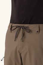 Close-up of a person wearing the 686 Men's Anything Cargo Pant - Slim Fit, featuring 13 pockets, front drawstring tie, button, belt loops, and a left zipper pocket. Paired with a black shirt for versatile outdoor style and functionality. Brand: 686.
