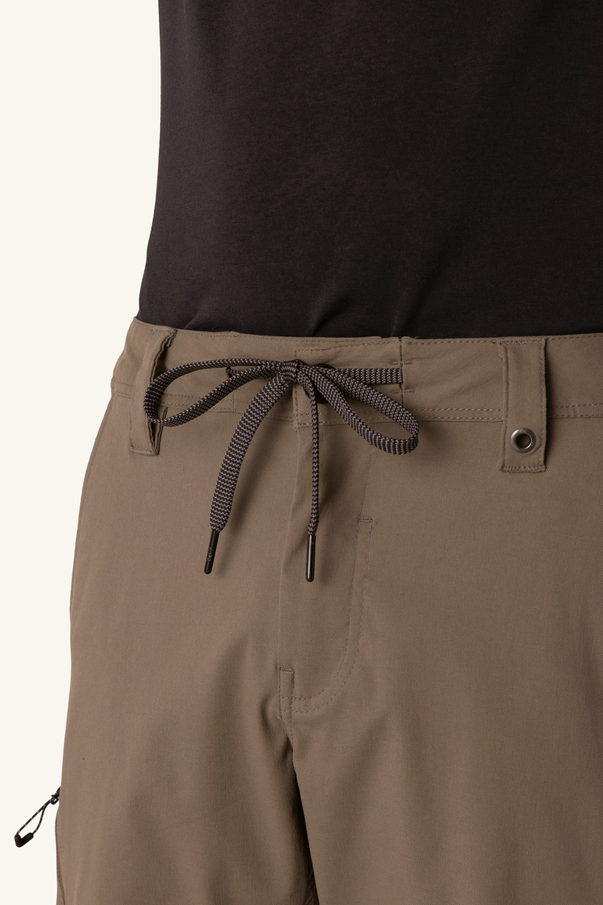 Close-up of a person wearing the 686 Men's Anything Cargo Pant - Slim Fit, featuring 13 pockets, front drawstring tie, button, belt loops, and a left zipper pocket. Paired with a black shirt for versatile outdoor style and functionality. Brand: 686.