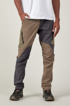 Wearing a white t-shirt and 686 Men's Anything Cargo Pant - Slim Fit by 686 in gray, brown, and olive, paired with black hiking shoes, a person stands with one hand in their pocket against a plain background, ready for adventure.