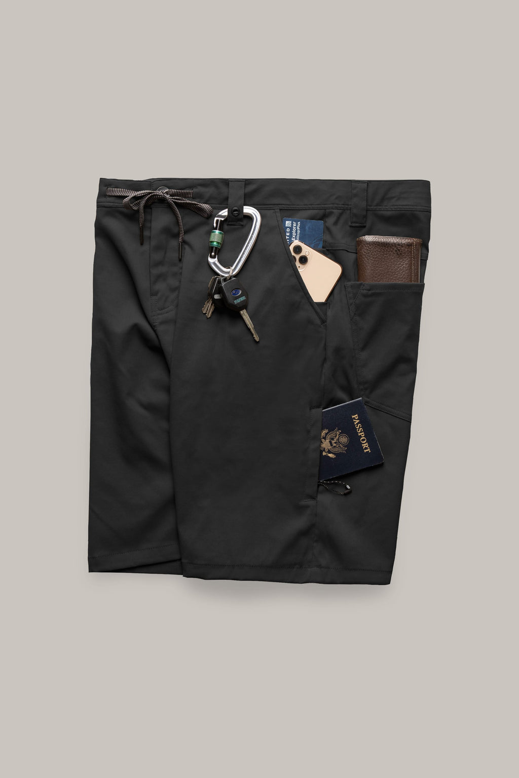 The 686 Men's Everywhere® Hybrid Short - Relaxed Fit by 686 is shown in black, featuring multiple pockets holding a wallet, keys on a carabiner, smartphone, and blue passport against a gray background. These breathable shorts are ideal for travel.