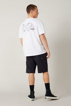 A person faces away, wearing a white tee with black globe and WAV graphic, 686 Men's Everywhere® Hybrid Short - Relaxed Fit, black socks, and black high-top sneakers against a plain background.