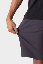 A person wearing a dark shirt and 686 Men's Everywhere® Hybrid Short - Relaxed Fit in dark gray stretches the fabric outward with their left hand, showcasing the shorts’ impressive flexibility.