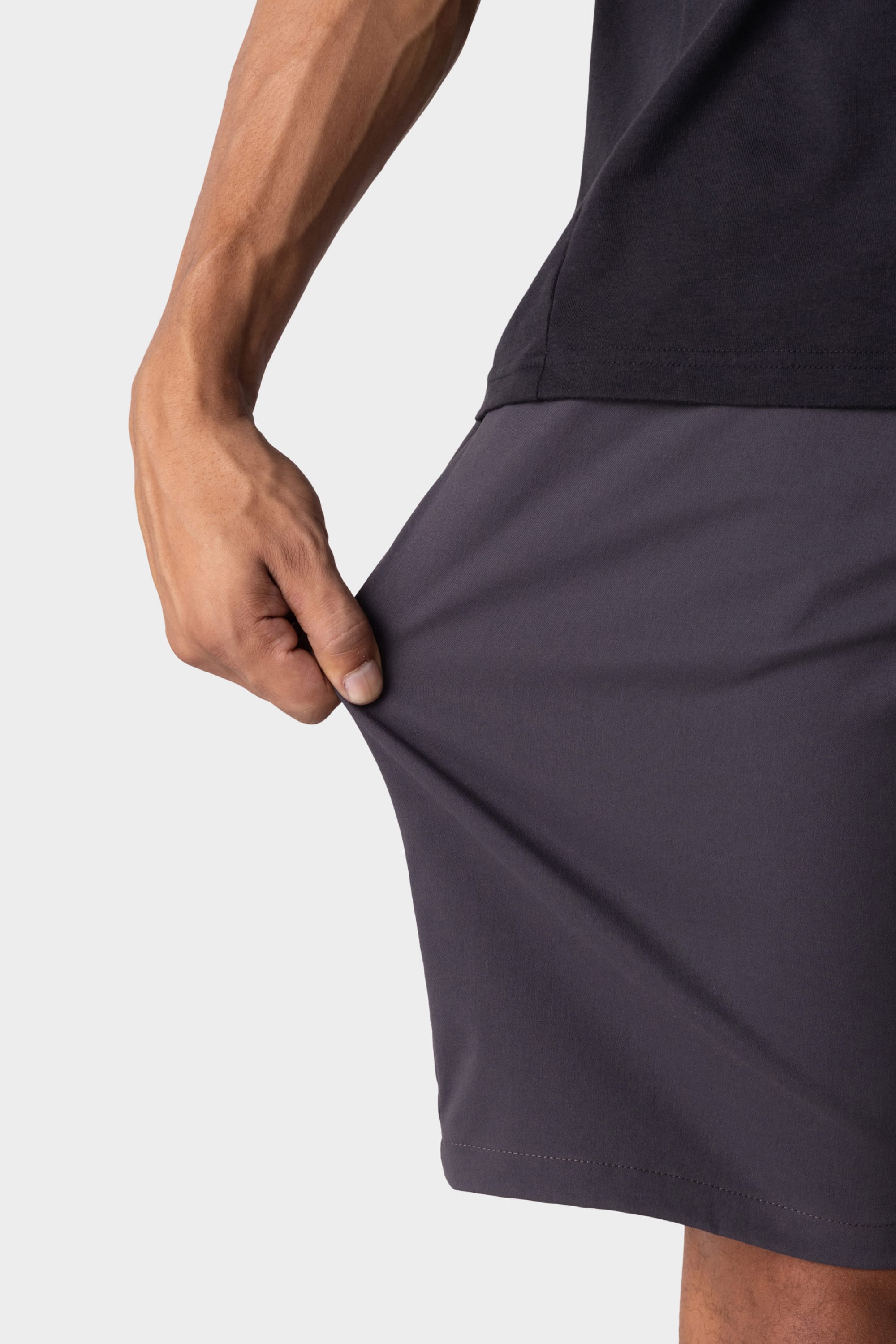 A person wearing a dark shirt and 686 Men's Everywhere® Hybrid Short - Relaxed Fit in dark gray stretches the fabric outward with their left hand, showcasing the shorts’ impressive flexibility.
