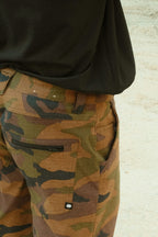 Close-up of a person wearing the 686 Men's Everywhere® Hybrid Short - Relaxed Fit in a camo pattern with a black shirt. The back pocket and waistband are highlighted against a neutral, light background. Brand: 686.