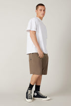 A young man stands sideways, looking at the camera. He wears a plain white t-shirt, 686 Men's Everywhere® Hybrid Short - Relaxed Fit by 686, black crew socks, and black high-top Converse sneakers against a neutral background.