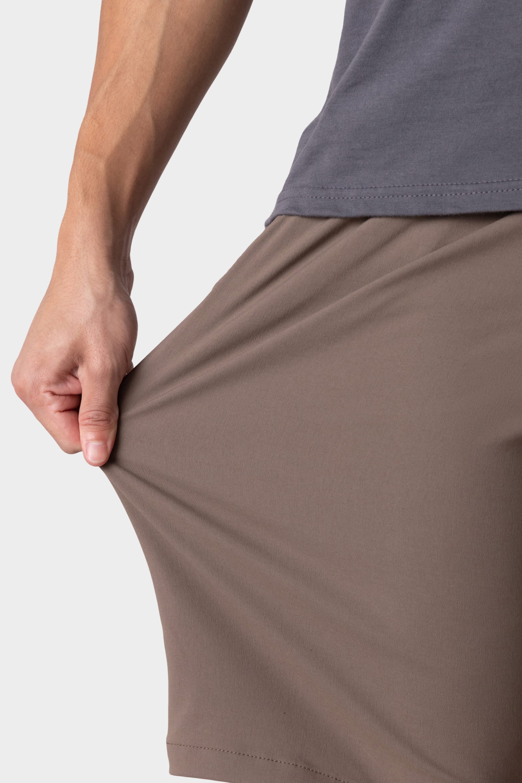 A person wearing a gray shirt and 686 Men's Everywhere® Hybrid Short - Relaxed Fit stretches the shorts' fabric outward with their left hand, demonstrating the flexibility of this 686 hybrid short.