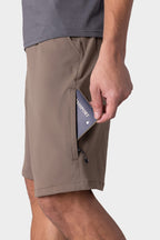 Wearing the 686 Men's Everywhere® Hybrid Short - Relaxed Fit, a person slips a passport into the zippered side pocket, with only their lower body and hand visible against a plain background.