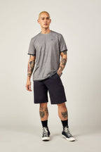 A man with short blond hair and tattoos wears the 686 Men's Let's Go Tech Tee, black shorts, socks, and sneakers, standing against an off-white background—perfectly outfitted by 686 for spring-summer adventures.