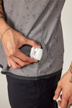 A person wearing the 686 Men's Let's Go Tech Tee and black pants puts a white wireless earbud case into a side pocket.