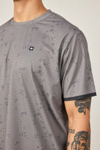 A person wearing the 686 Men's Let's Go Tech Tee—a gray, breathable shirt with a small round chest logo—perfect for spring and summer adventures. They also have a tattoo of a snarling animal on their arm.