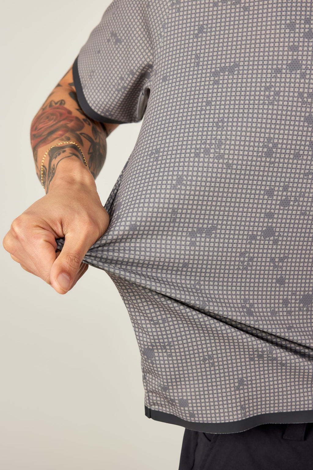 A tattooed model stretches the 686 Men's Let's Go Tech Tee, highlighting its lightweight, stretchy, and breathable fabric—ideal for spring and summer adventures—against a plain light background.