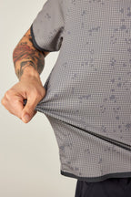A tattooed model stretches the 686 Men's Let's Go Tech Tee, highlighting its lightweight, stretchy, and breathable fabric—ideal for spring and summer adventures—against a plain light background.