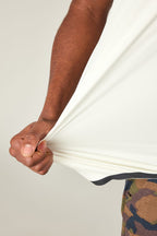 A person with medium brown skin stretches the bottom of the 686 Men's Let's Go Tech Tee. Only their arm, torso, and hand are visible. Paired with camouflage pants, this lightweight tee by 686 is ready for any spring or summer adventure.