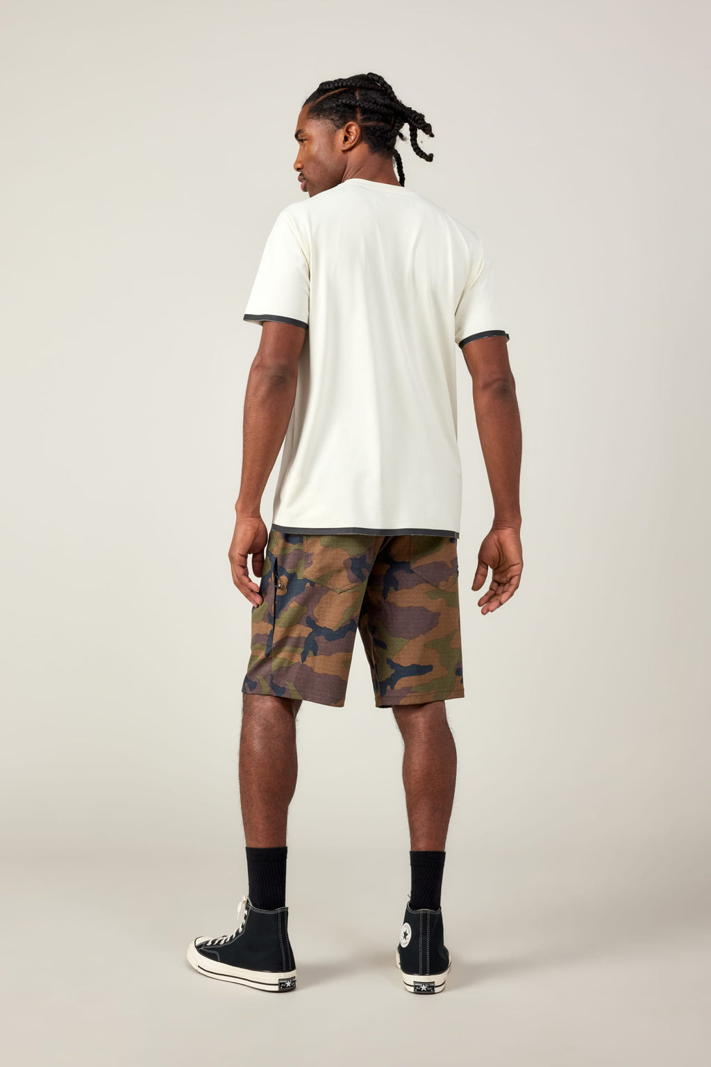 A man stands facing away in the 686 Men's Let's Go Tech Tee, paired with camouflage shorts, black crew socks, and high-top sneakers—an ideal spring-summer adventure look against a plain light background.