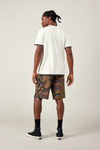 A man stands facing away in the 686 Men's Let's Go Tech Tee, paired with camouflage shorts, black crew socks, and high-top sneakers—an ideal spring-summer adventure look against a plain light background.