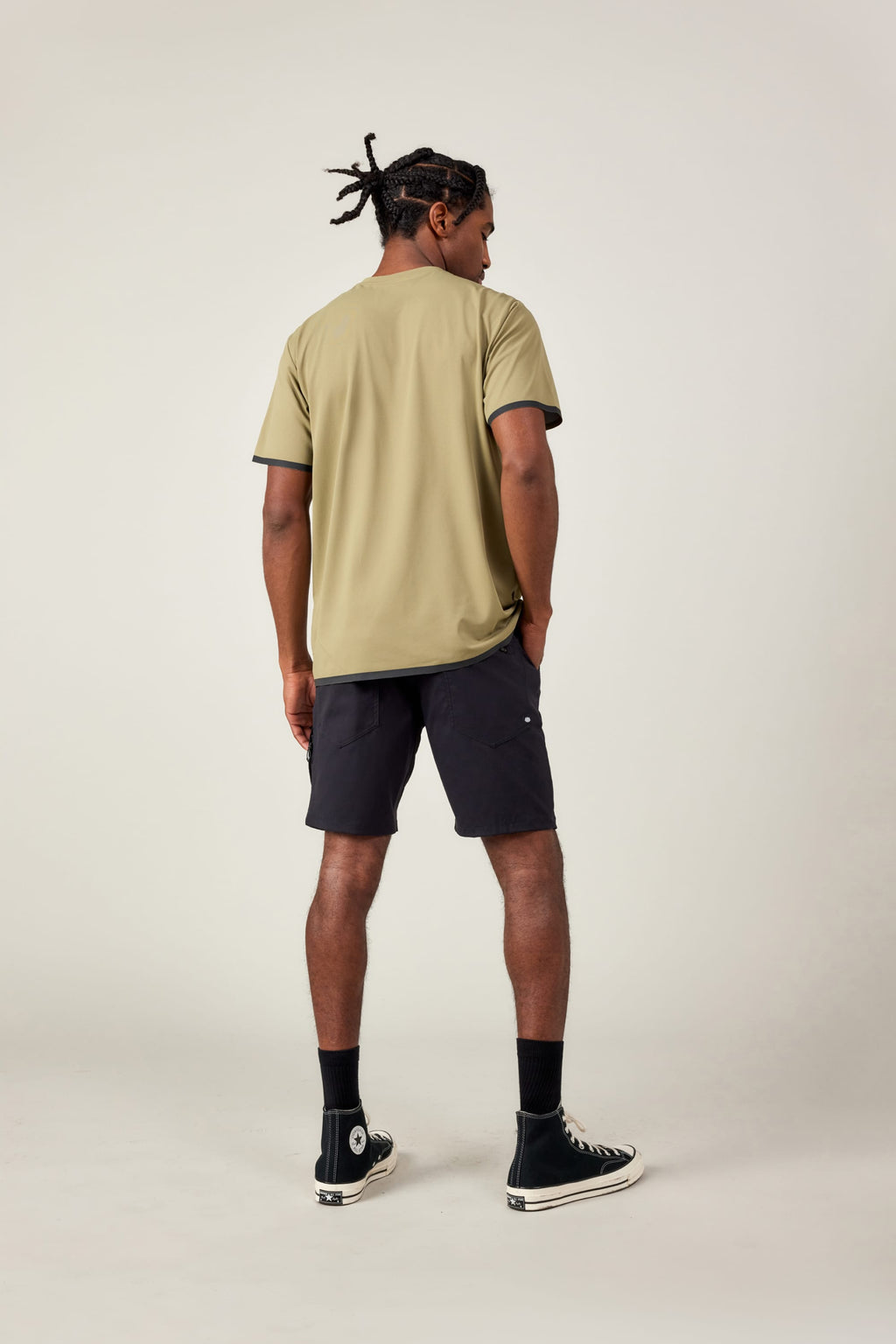 A man faces away from the camera in a 686 Men's Let's Go Tech Tee, black shorts, socks, and high-top sneakers against a plain light background—ideal for spring and summer adventures.