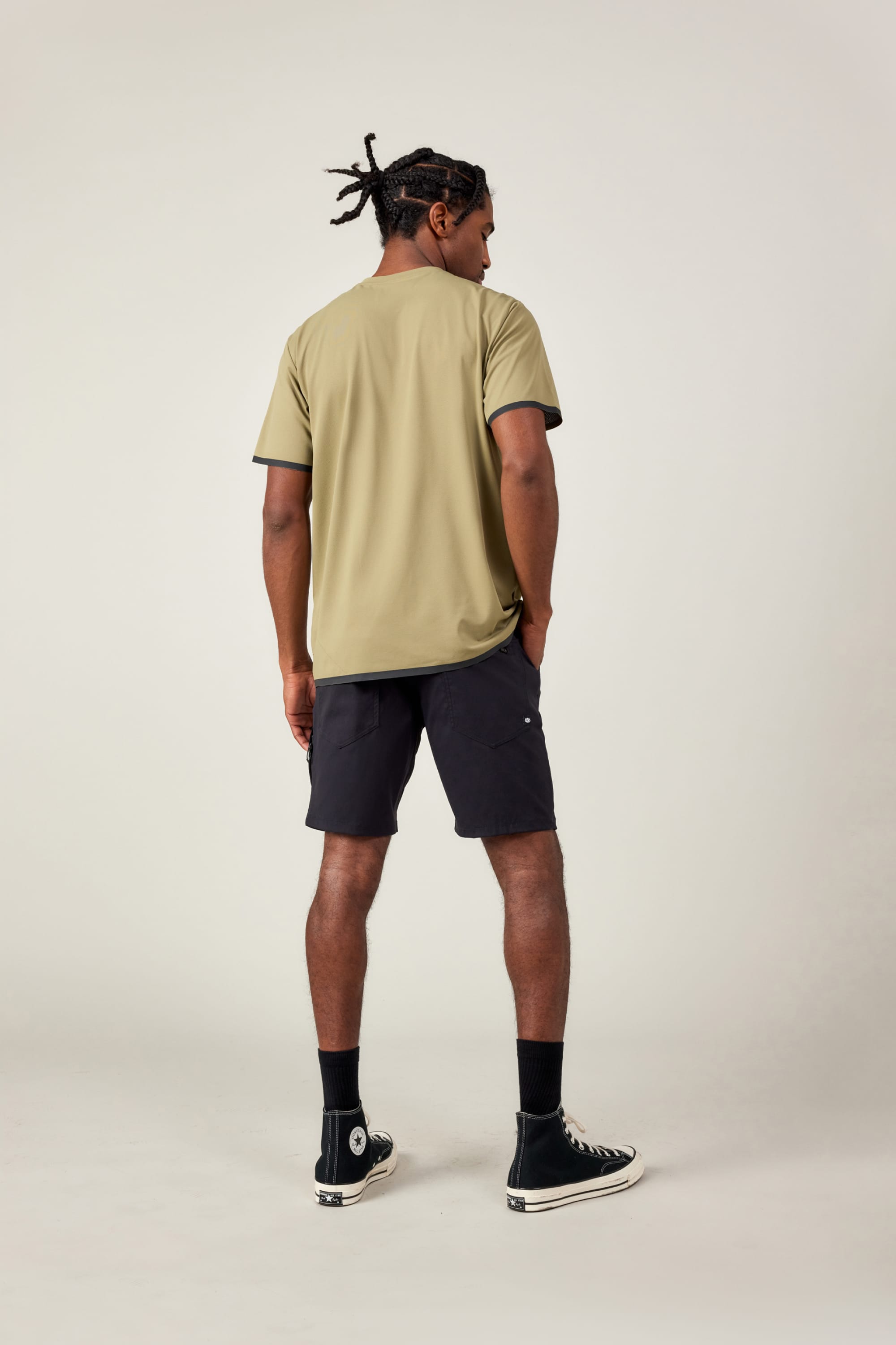 A man faces away from the camera in a 686 Men's Let's Go Tech Tee, black shorts, socks, and high-top sneakers against a plain light background—ideal for spring and summer adventures.