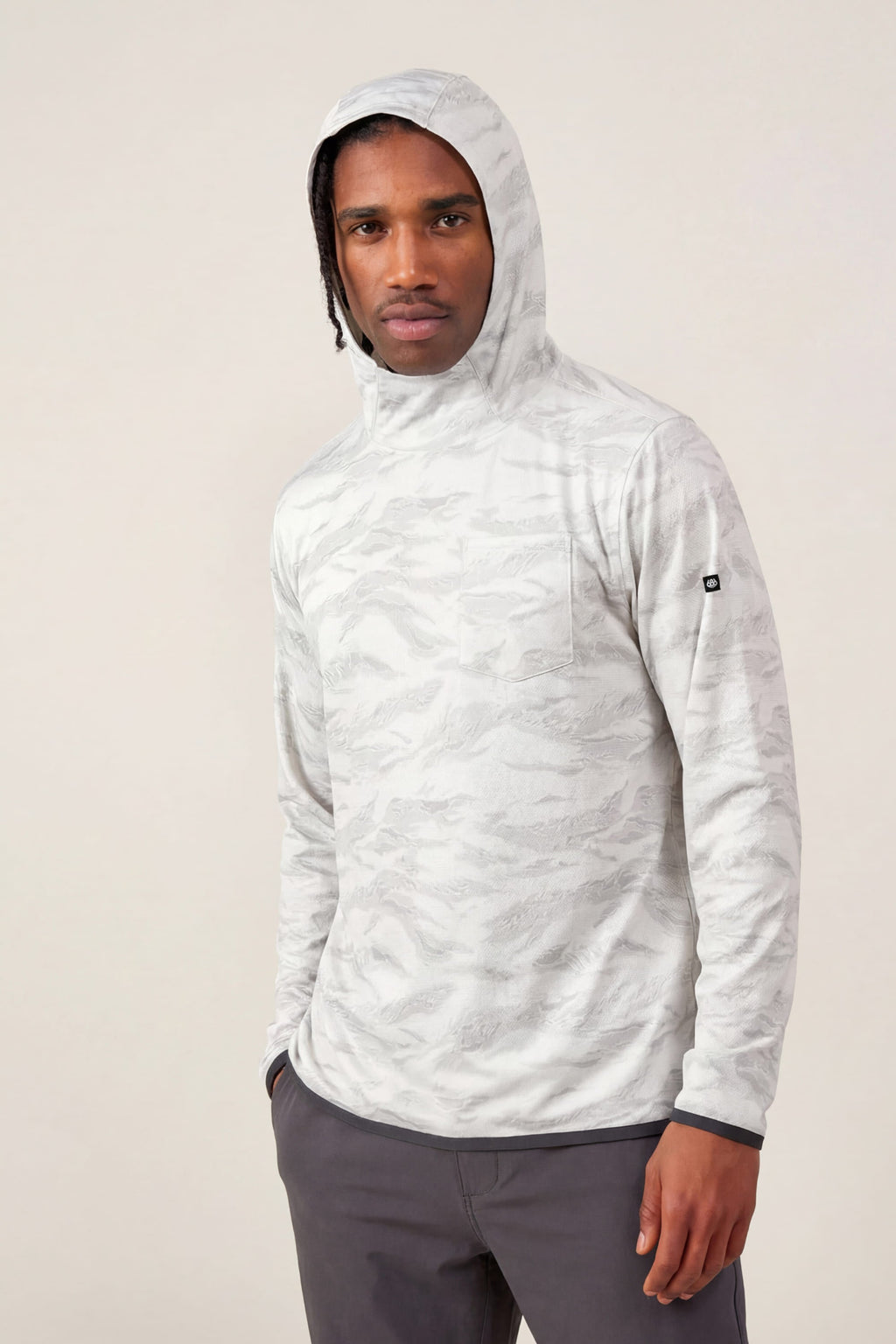 A man in the 686 Men's Let's Go Tech Hoody and dark gray pants stands against a plain light background, looking at the camera with a neutral expression—the perfect sun protection from 686 for any setting.