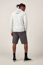 A man with braided hair faces away, wearing the 686 Men's Let's Go Tech Hoody in light gray, paired with dark gray knee-length shorts, black socks, and black high-top sneakers against a plain light background.