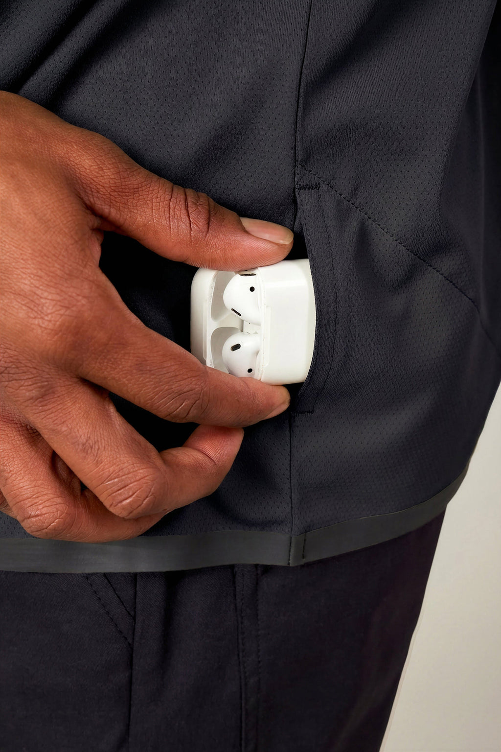 A person puts a white wireless earbud case with earbuds into the side pocket of dark athletic pants while wearing the 686 Men's Let's Go Tech Hoody by 686 for added comfort.
