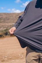 A person outdoors stretches the hem of their 686 Men's Let's Go Tech Hoody, with a dry, hilly landscape and blue sky in the background.