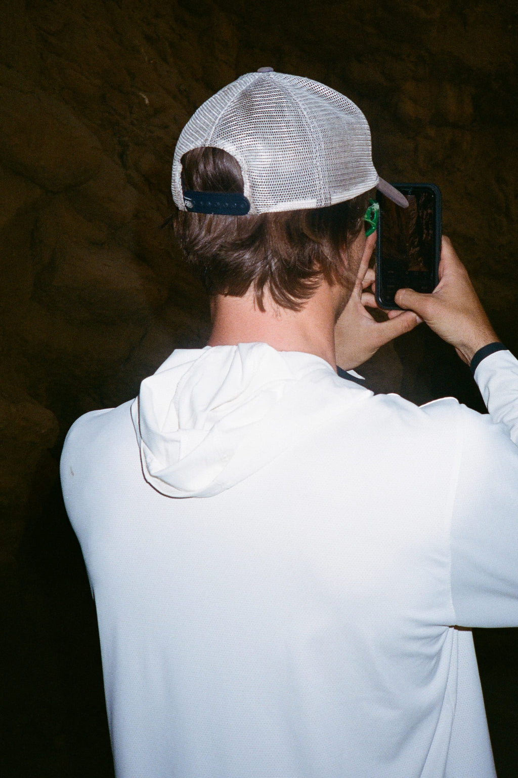 Wearing the 686 Mens Lets Go Tech Hoody, a person is seen from behind taking a photo with their smartphone against a dark, rocky background.