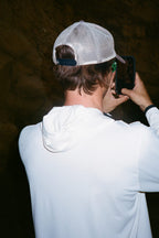 Wearing the 686 Mens Lets Go Tech Hoody, a person is seen from behind taking a photo with their smartphone against a dark, rocky background.