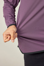 A hand pinches and stretches the side of a 686 Mens Lets Go Tech Hoody, highlighting its purple color, lightweight fabric, and flexibility. The lower arm and hand are shown for detail. Brand: 686.
