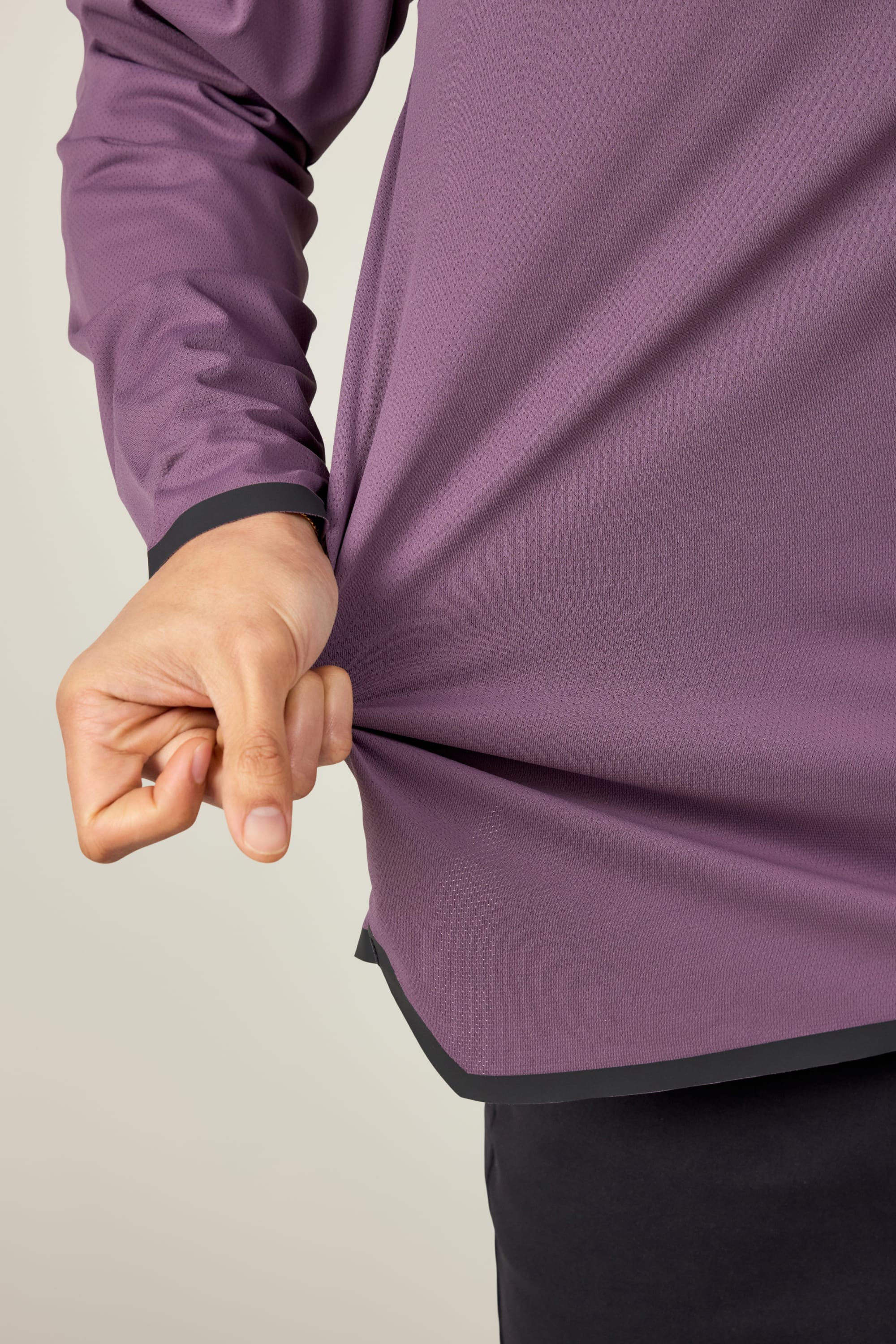 A hand pinches and stretches the side of a 686 Mens Lets Go Tech Hoody, highlighting its purple color, lightweight fabric, and flexibility. The lower arm and hand are shown for detail. Brand: 686.