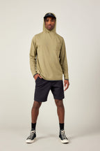 A man faces forward against a plain light background, wearing the 686 Mens Lets Go Tech Hoody in khaki for sun protection, paired with black shorts, socks, sneakers, and a dark visor cap.