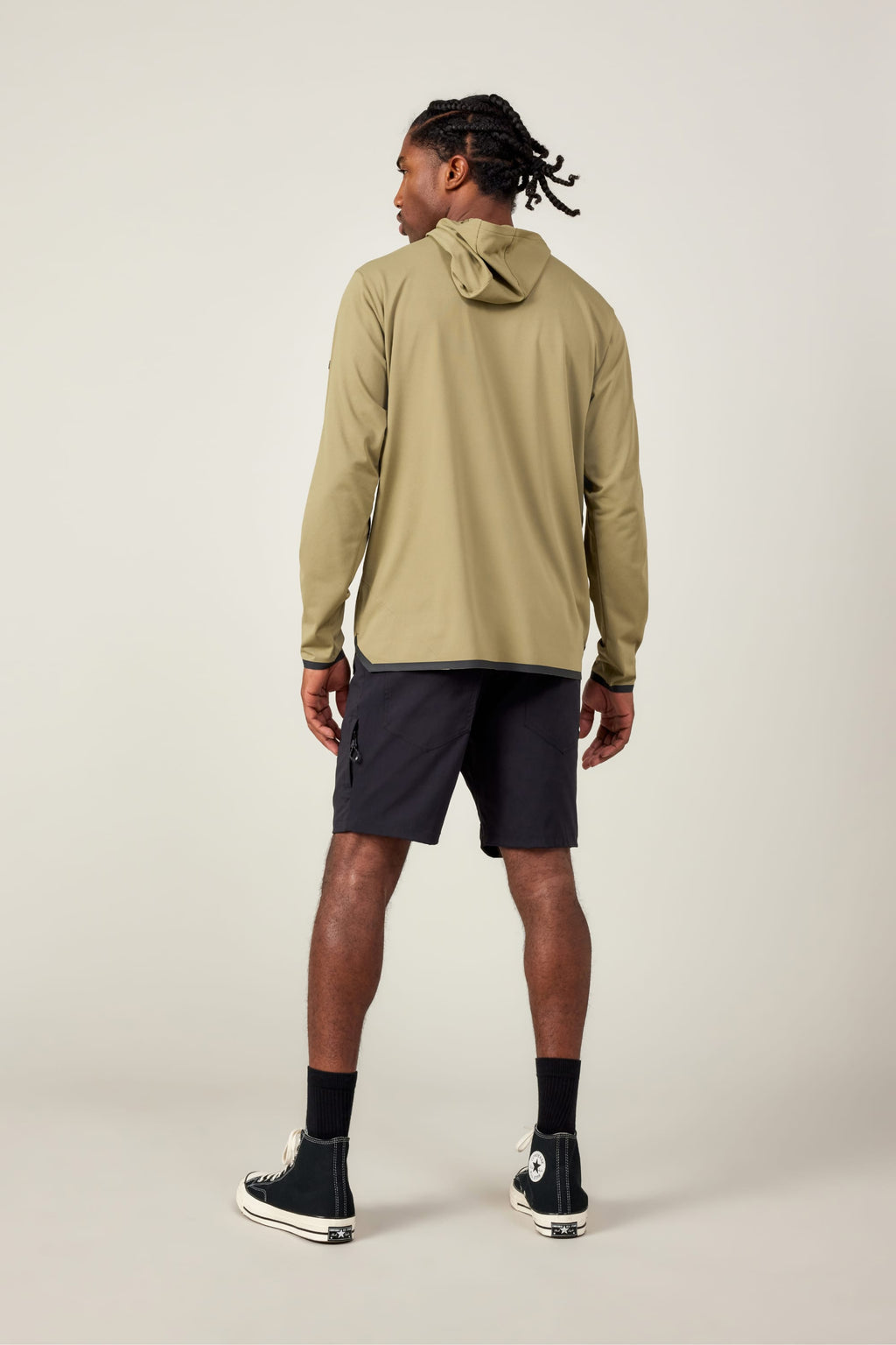 A person stands facing away, wearing the 686 Mens Lets Go Tech Hoody in light olive green for sun protection, paired with black shorts, socks, and high-top sneakers with white soles, against a plain light background.