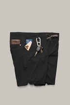 A pair of 686 Men's Everywhere® Featherlight Chino Shorts in black, with a brown leather wallet, a smartphone in a tan case, a blue access card, keys on a carabiner, and a brown braided belt tucked into the waistband and pockets.
