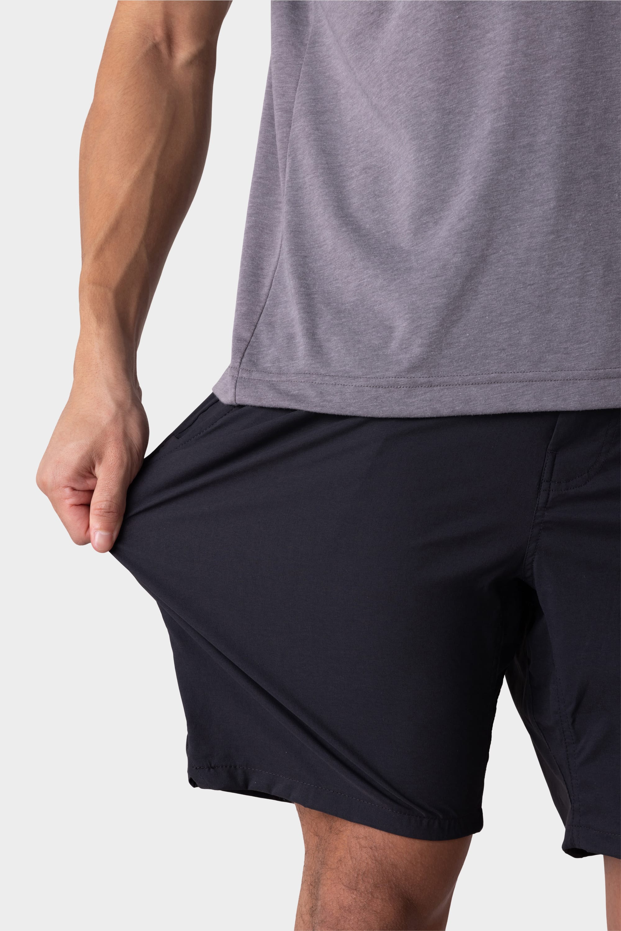 A person wearing a gray shirt and 686 Men's Everywhere® Featherlight Chino Short stretches the shorts' fabric with one hand, demonstrating the flexibility of the 686 brand material.