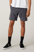 A person wears the 686 Men's Everywhere® Featherlight Chino Short in dark gray, paired with a white T-shirt, black crew socks, and black slip-on shoes, standing with hands in pockets, pictured from mid-torso to feet on a plain background.