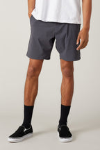 The lower half of a person is shown wearing 686 Men's Everywhere® Featherlight Chino Short, a white T-shirt, black crew socks, and black slip-on shoes, standing against a plain light background.