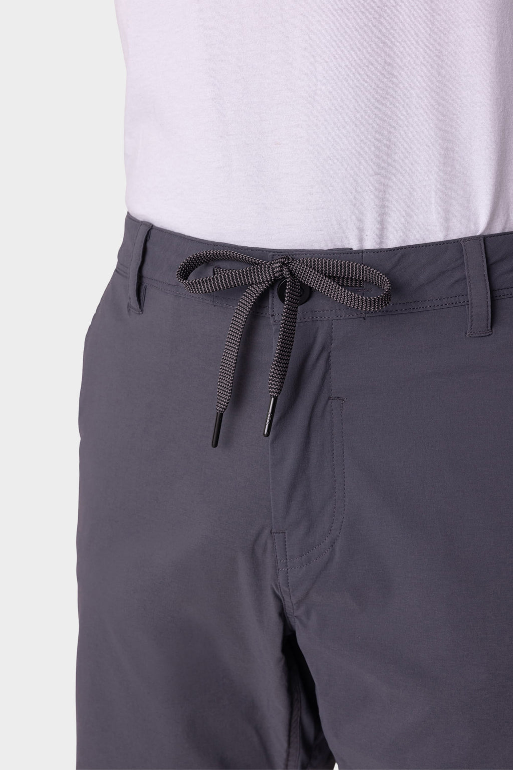 A close-up shows a person wearing 686 Men's Everywhere® Featherlight Chino Shorts in dark gray with a drawstring tie, paired with a white shirt tucked in. Only the waist and upper legs are visible. Brand: 686.