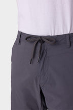 A close-up shows a person wearing 686 Men's Everywhere® Featherlight Chino Shorts in dark gray with a drawstring tie, paired with a white shirt tucked in. Only the waist and upper legs are visible. Brand: 686.