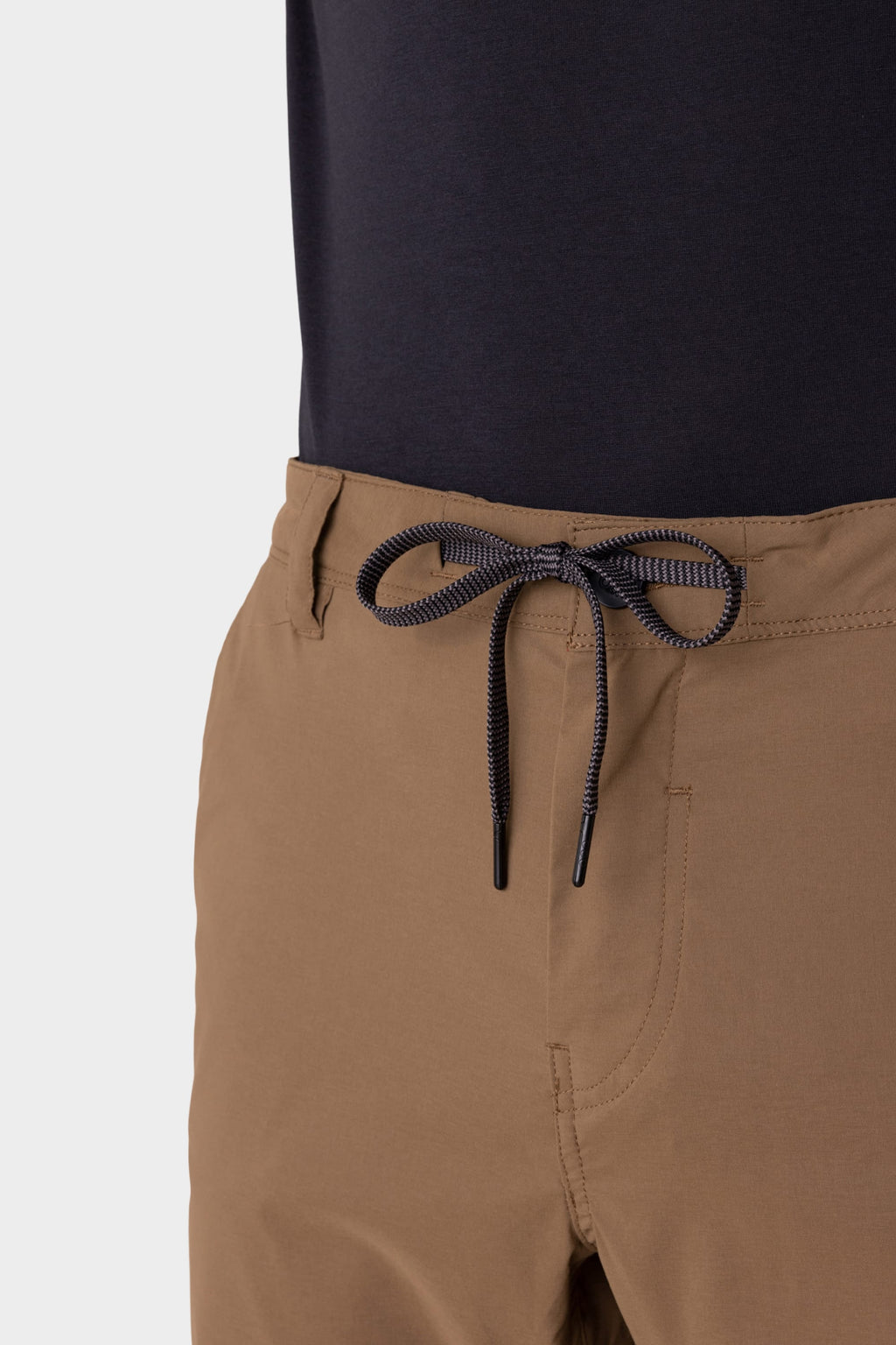 A close-up of a person wearing 686 Men's Everywhere® Featherlight Chino Shorts in light brown with a drawstring waistband and a dark shirt, focusing on the neatly tied drawstring.