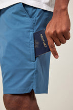 A person wearing 686 Men's Everywhere® Featherlight Chino Shorts in blue places a navy passport into the side pocket, with part of a white shirt visible above.