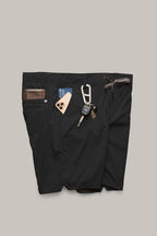 A pair of 686 Men's Everywhere® Featherlight Chino Shorts in black holds a brown wallet, smartphone, keys on a carabiner, and a card in its waistband and pockets against a light gray background.