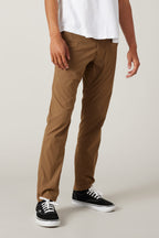 A person wears a white t-shirt, 686 Men's Everywhere® Featherlight Chino Pant - Slim Fit in light brown, and black low-top sneakers against a plain background. The lightweight chinos are ideal for summer style. Upper body is mostly out of frame.