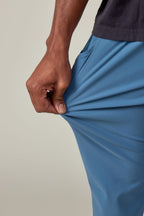 A person wearing 686 Men's Everywhere® Featherlight Chino Pant - Slim Fit demonstrates the lightweight, flexible fabric by stretching it with one hand—ideal for a breathable summer look.