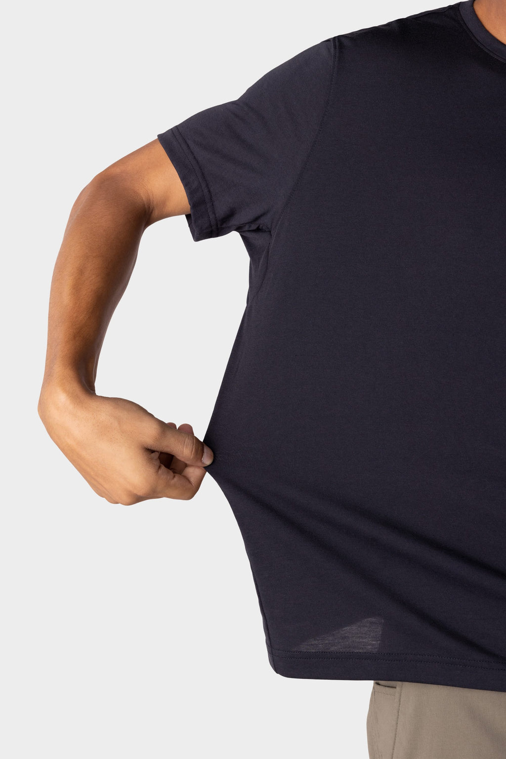 A person wearing the 686 Mens Everywhere drirelease® Tech Tee stretches the side of the dark short-sleeve shirt with one hand, showcasing its flexible fabric. Only their upper body and arm are visible against a plain background.