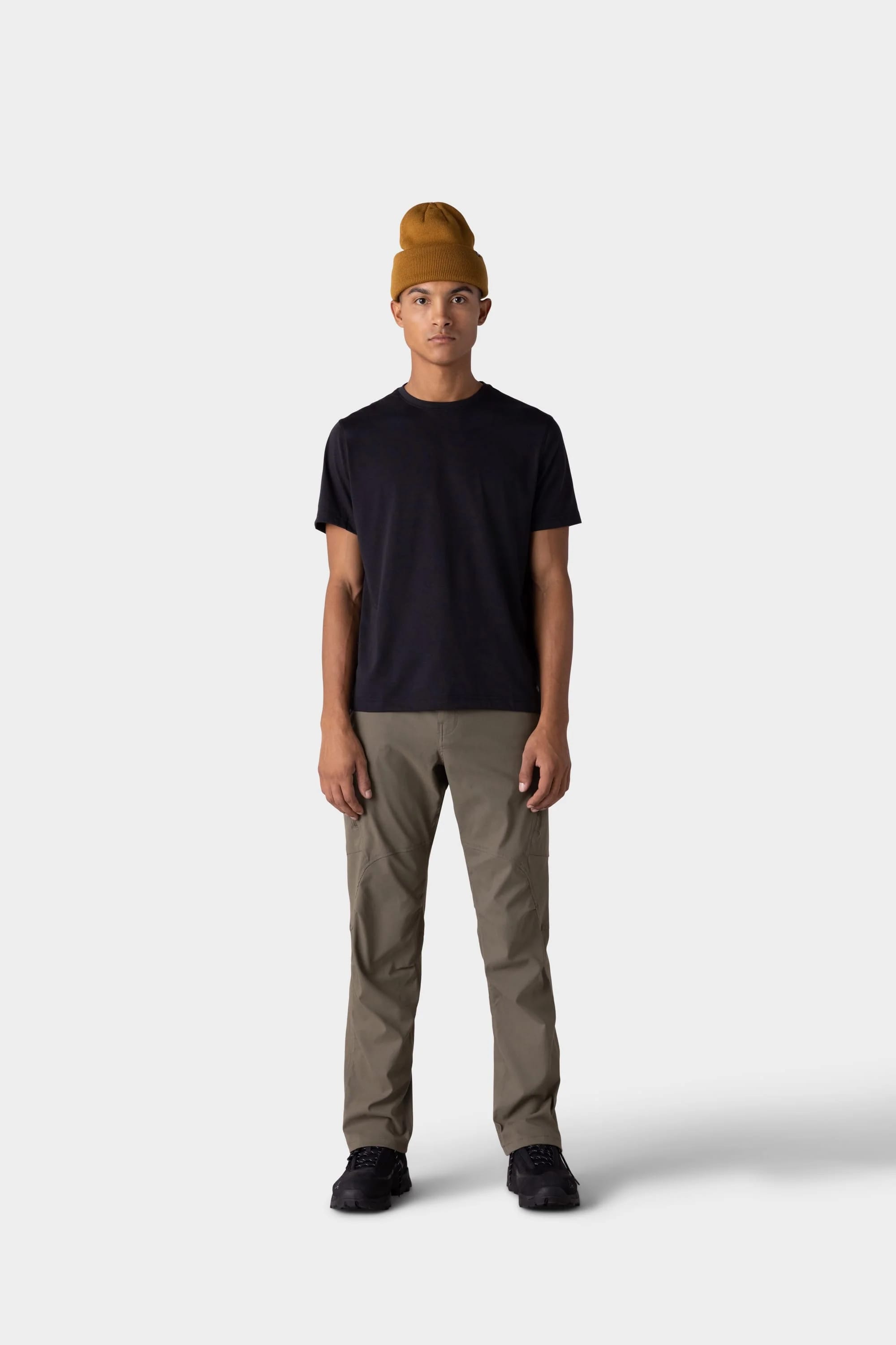 A person stands against a plain light gray background, wearing a mustard yellow beanie, olive green pants, black shoes, and the 686 Mens Everywhere drirelease® Tech Tee by 686. They face forward with a neutral expression.