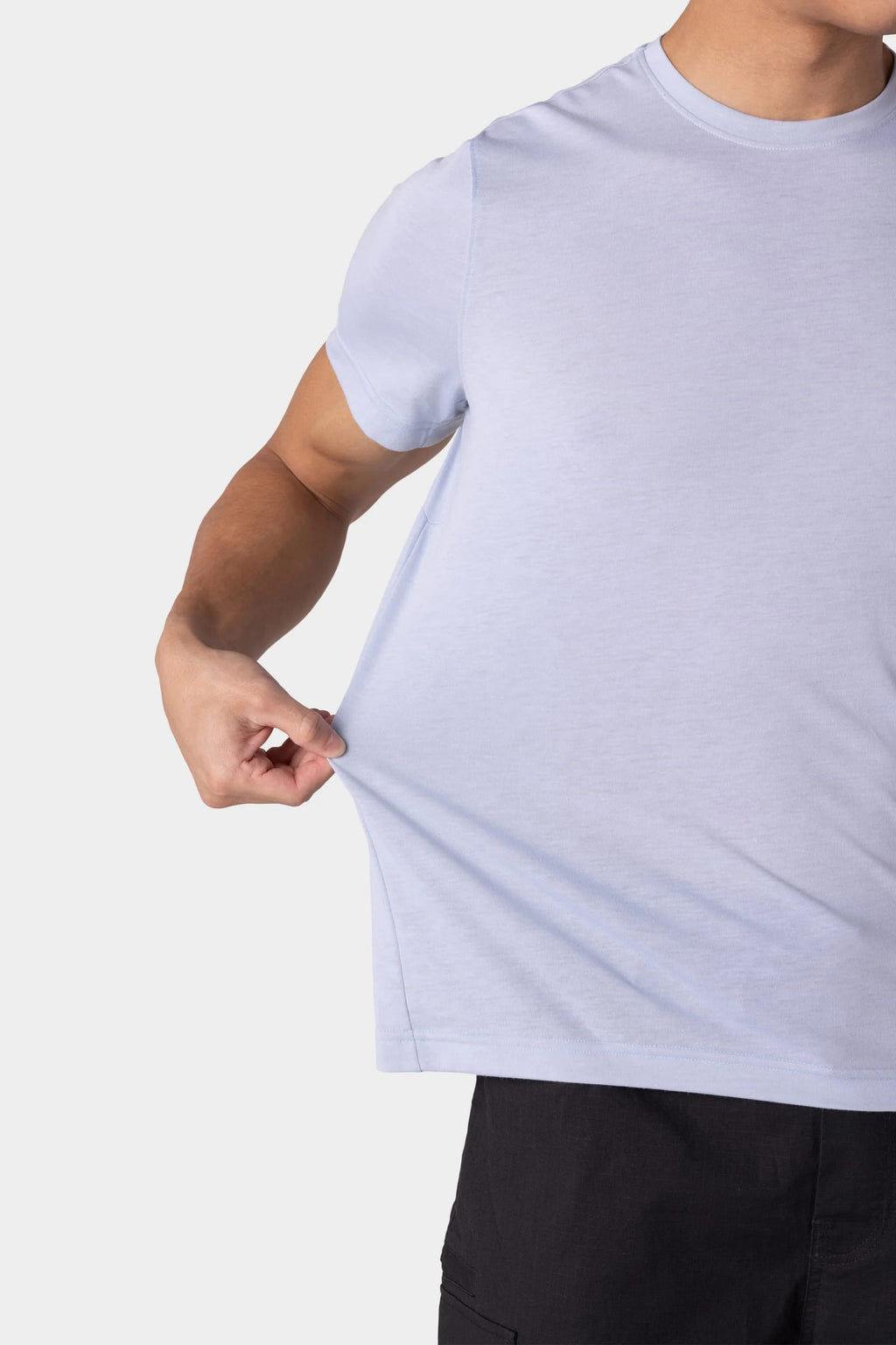 A person demonstrates the flexibility of the 686 Mens Everywhere drirelease® Tech Tee by stretching its light blue fabric with one hand. Their head is not visible, and they are wearing black pants.